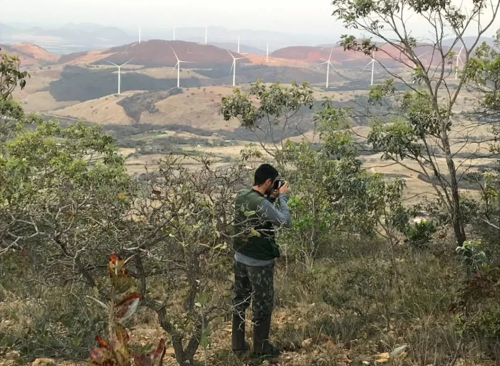 Técnico registrando imagens de campo com parque eólico ao fundo